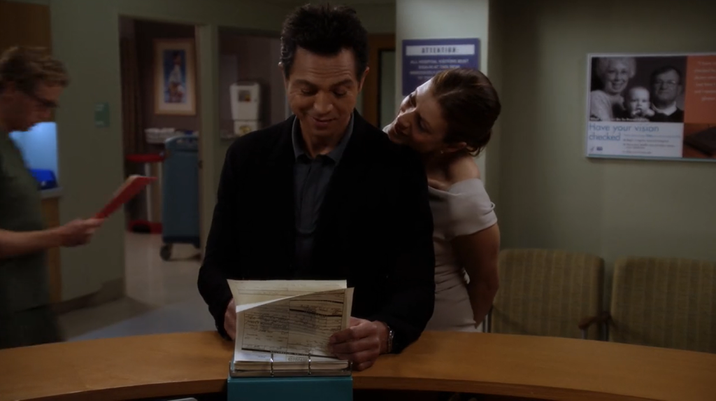 Still of Jake (played by Benjamin Bratt) reading Amelia's (played by Caterina Scorsone) (not pictured) chart while Addison (played by Kate Walsh) tries to read the chart while she rests her chin on his shoulder from Private Practice 5x22